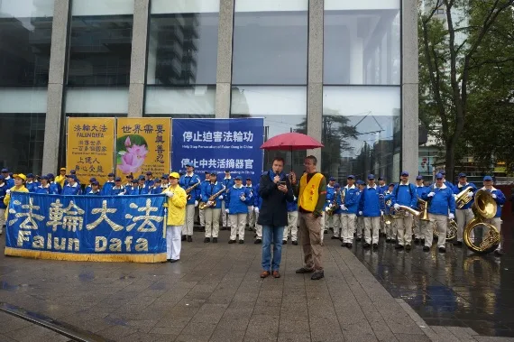 Kundgebung der European Tian Guo Marching Band im Regen, mit Transparenten gegen die Verfolgung von Falun Gong in China, 2023