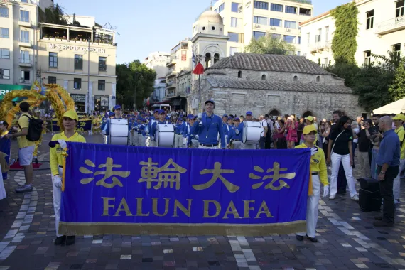 Parade der European Tian Guo Marching Band mit Falun-Dafa-Transparent auf dem Monastiraki-Platz vor der Pantanassa-Kirche in Athen, 2026