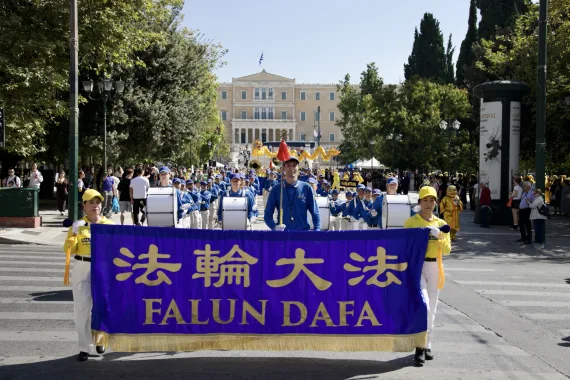Falun-Dafa-Transparent an der Spitze der European Tian Guo Marching Band, dahinter Drachentanz und das griechische Parlament am Syntagma-Platz in Athen, 2026