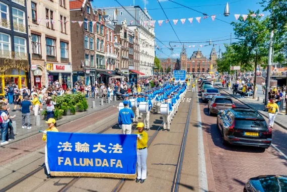 European Tian Guo Marching Band auf dem Damrak mit Blick zum Hauptbahnhof Amsterdam Centraal, 2025