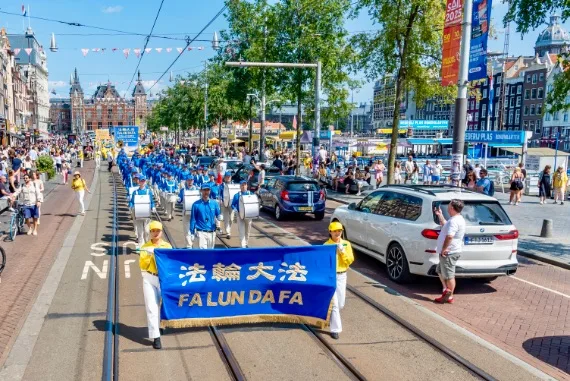 European Tian Guo Marching Band auf dem Damrak in Amsterdam, im Hintergrund der Hauptbahnhof, 2025