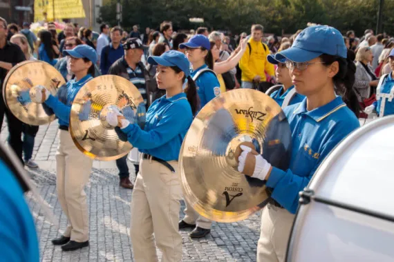 Beckenspiel der European Tian Guo Marching Band im Gleichschritt über Kopfsteinpflaster, umringt von Zuschauern